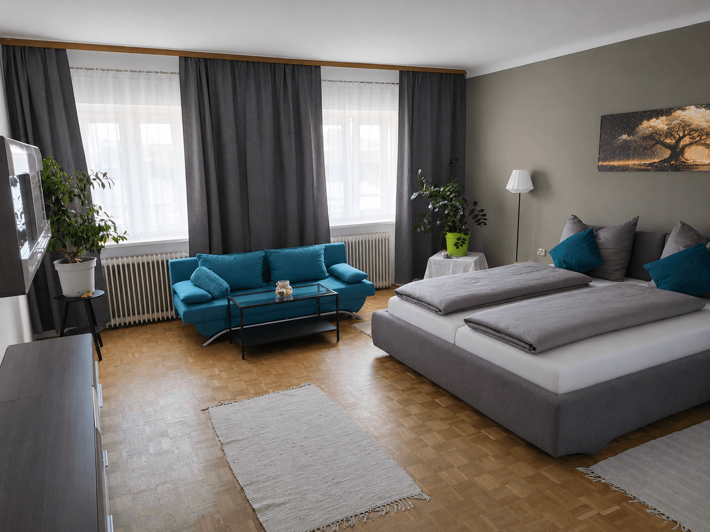 Suite Lebensbaum – Wohnbereich mit türkisem Sofa und Doppelbett